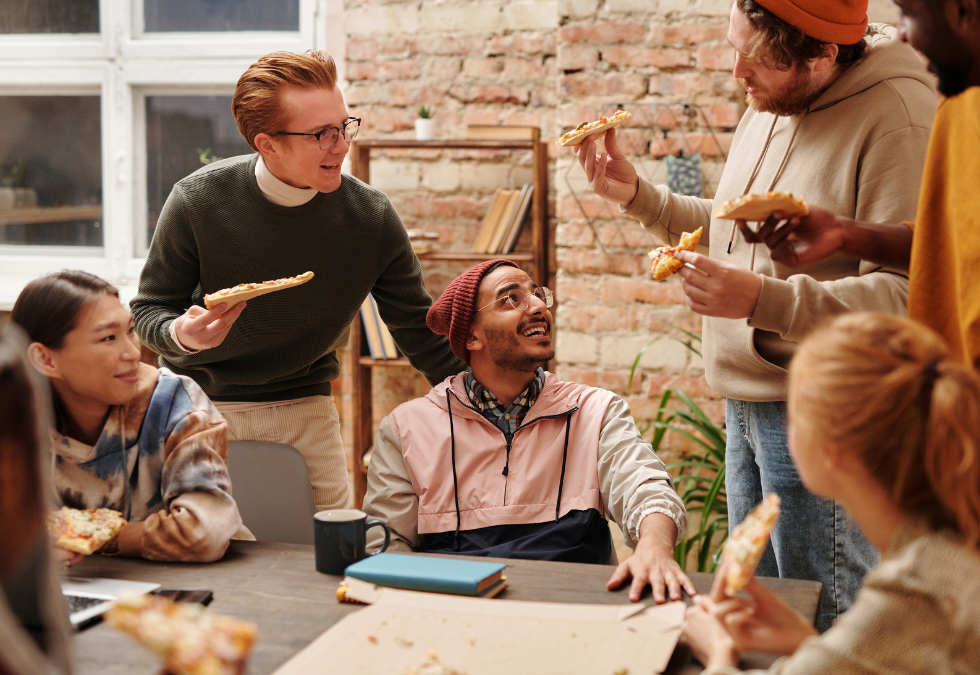 A group of coworkers having an inspiring meeting around a table with a rustic backdrop. They are smiling and making wide hand gestures.